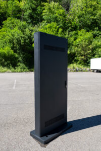 Rückseite eines digitalen Outdoor-Kundenstoppers im cleanen Design, mit nur einem sichtbaren Netzkabel. Zu sehen sind wetterfeste Lüftungsschlitze sowie ein dezenter Griff mit Schloss zum einfachen Öffnen des Gehäuses für die Wartung.