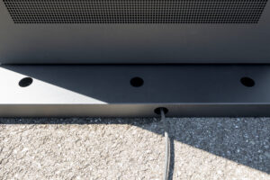 Nahaufnahme vom anthrazitfarbenen Sockel eines digitalen Outdoor-Kundenstoppers auf Asphalt, bei dem für ein sauberes Design nur ein einzelnes, schwarzes Netzkabel für den Stromanschluss dezent nach hinten herausgeführt wird.