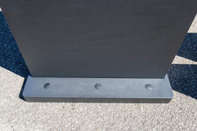 Nahaufnahme vom massiven, anthrazitfarbenen Standfuß einer digitalen Outdoor-Touchstehle auf Asphalt mit drei Abdeckungen an der Vorderseite.