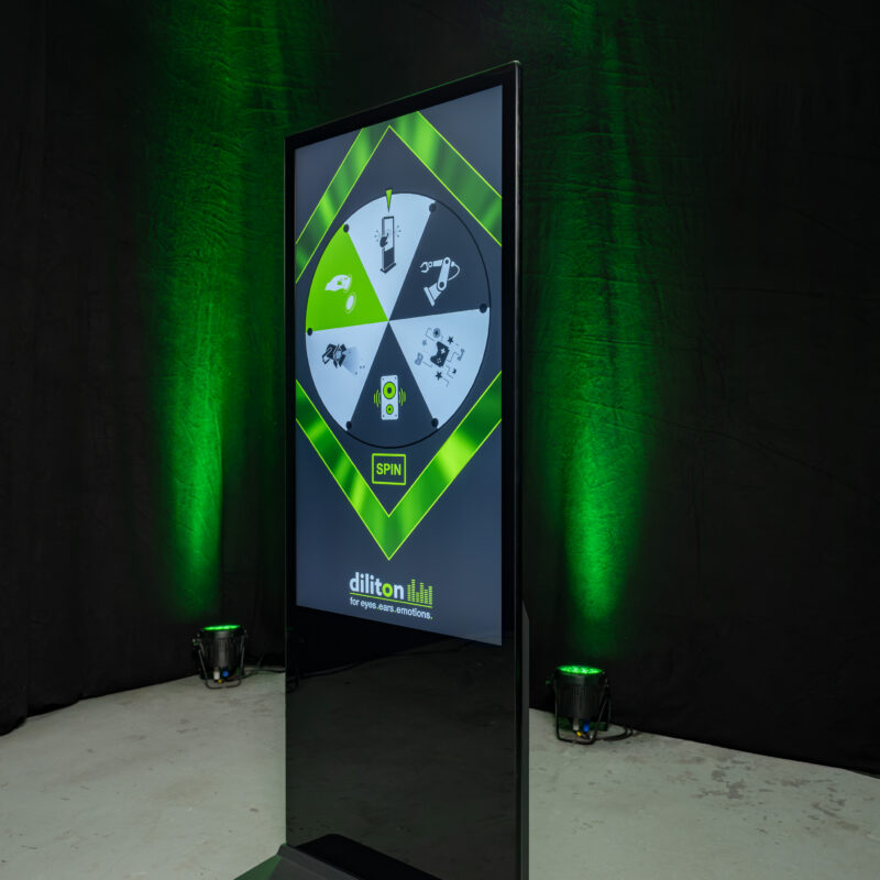 Digitale Touch-Stele von diliton mit einem interaktiven Glücksrad auf dem Bildschirm. Die schwarze Informationsstele steht vor einem dunkel abgehängten Hintergrund, der mit grünem Event-Licht von Floorspots angestrahlt wird.