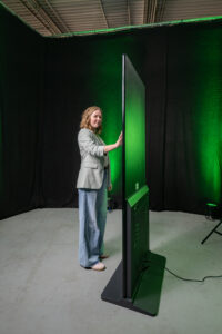 Das Bild zeigt die filigrane Seitenansicht der digitalen Touchstele während der Bedienung durch eine Person. Gut zu erkennen ist das extrem schlanke Profil des Gehäuses, welches vollständig aus robustem Stahl und Aluminium gefertigt ist.