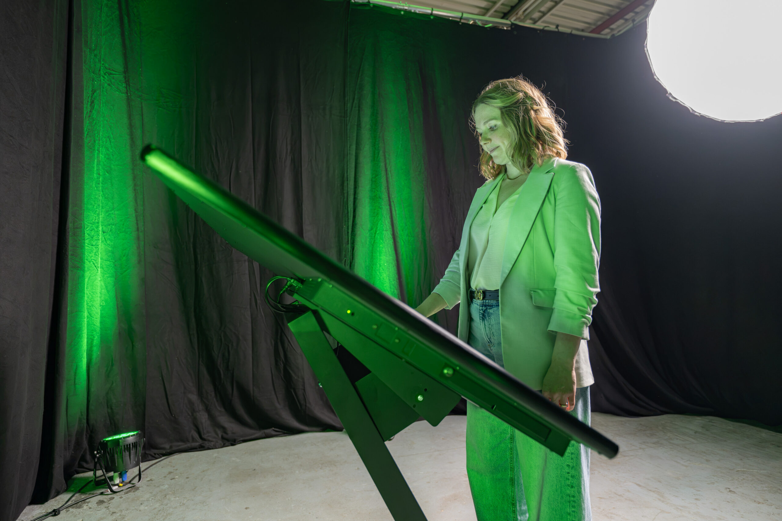 Seitenansicht einer Frau im hellen Blazer bei der Bedienung einer interaktiven Kiosk-Stele im Querformat mit einem geschwungenen S-Sockel Standfuß im Fotostudio.