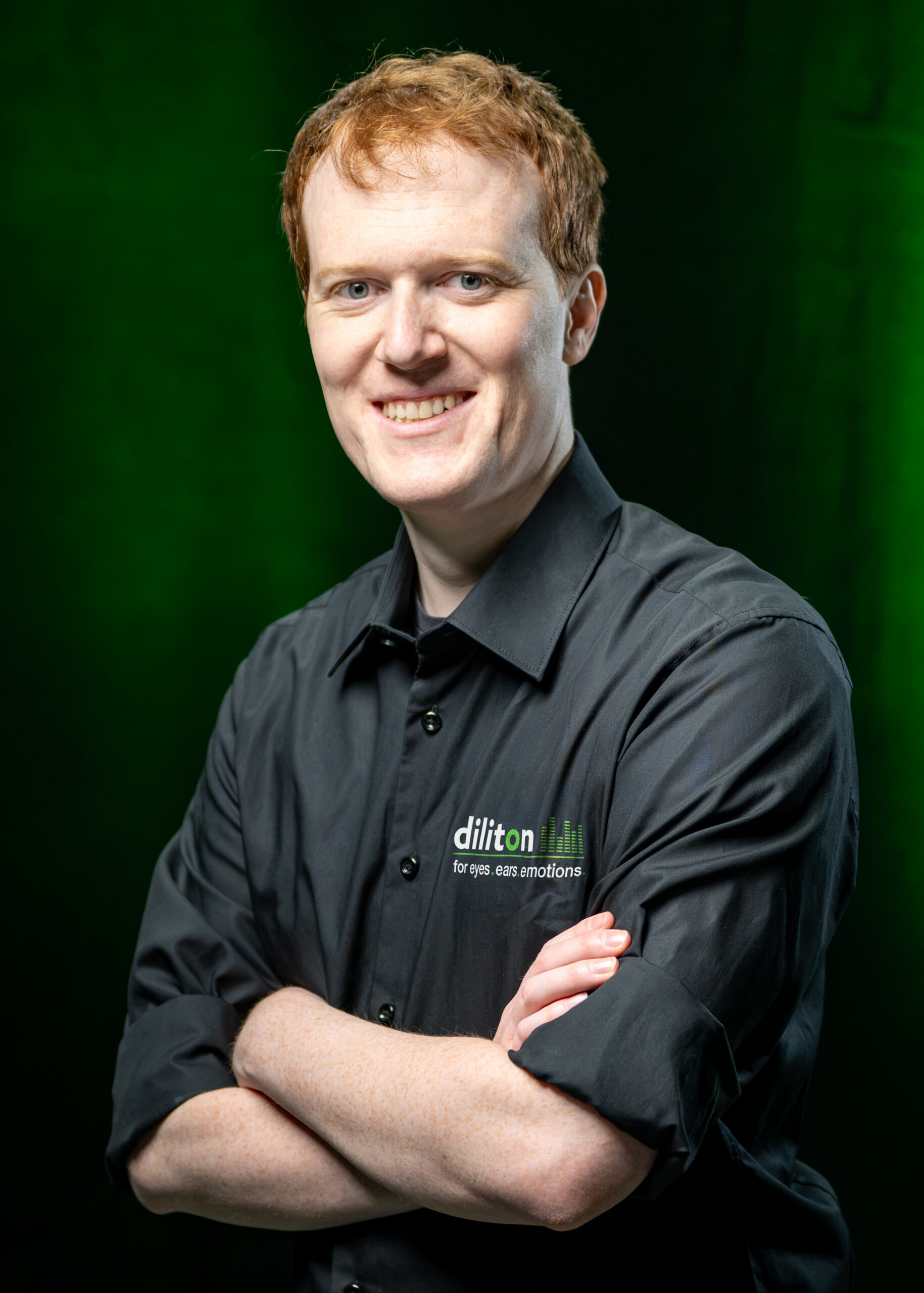 Porträt von Ian Pflumm, Mitarbeiter für Content Creation und Entwicklung bei diliton, im schwarzen Firmenhemd vor grünem Hintergrund.