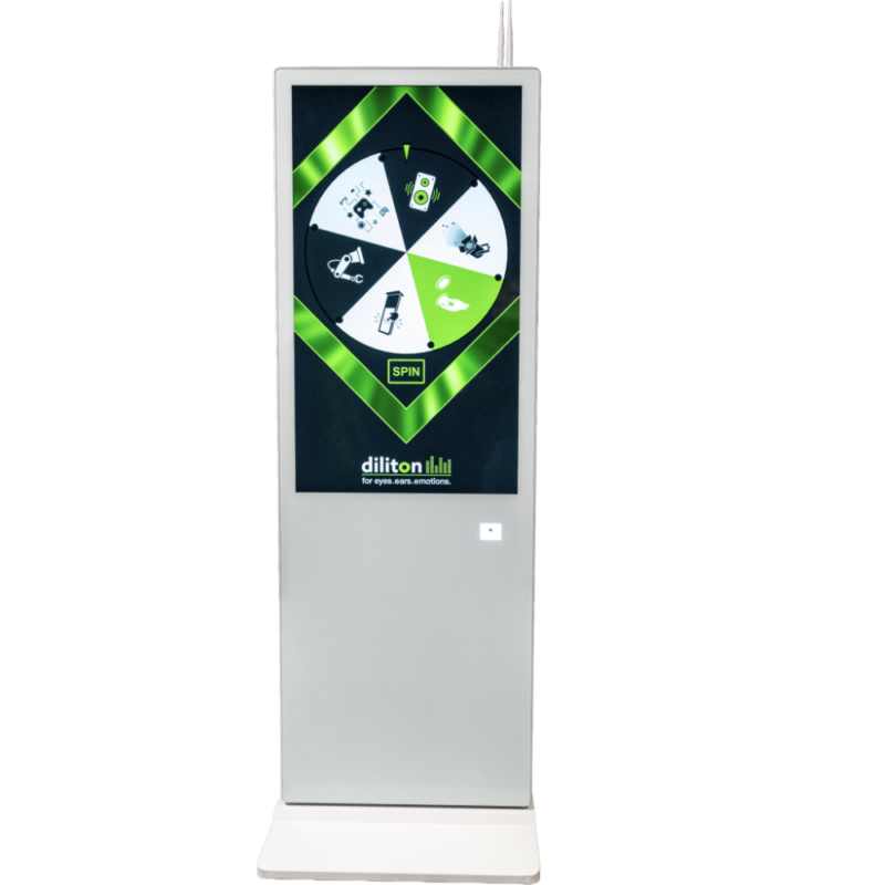 Eine freistehende, weiße digitale Touch-Stele mit einem großen Hochkant-Bildschirm. Auf dem Display ist eine interaktive Glücksrad-App mit grünem Grafikdesign und dem Logo „diliton“ zu sehen. Am oberen Rand der Stele sind zwei kleine Antennen angebracht.