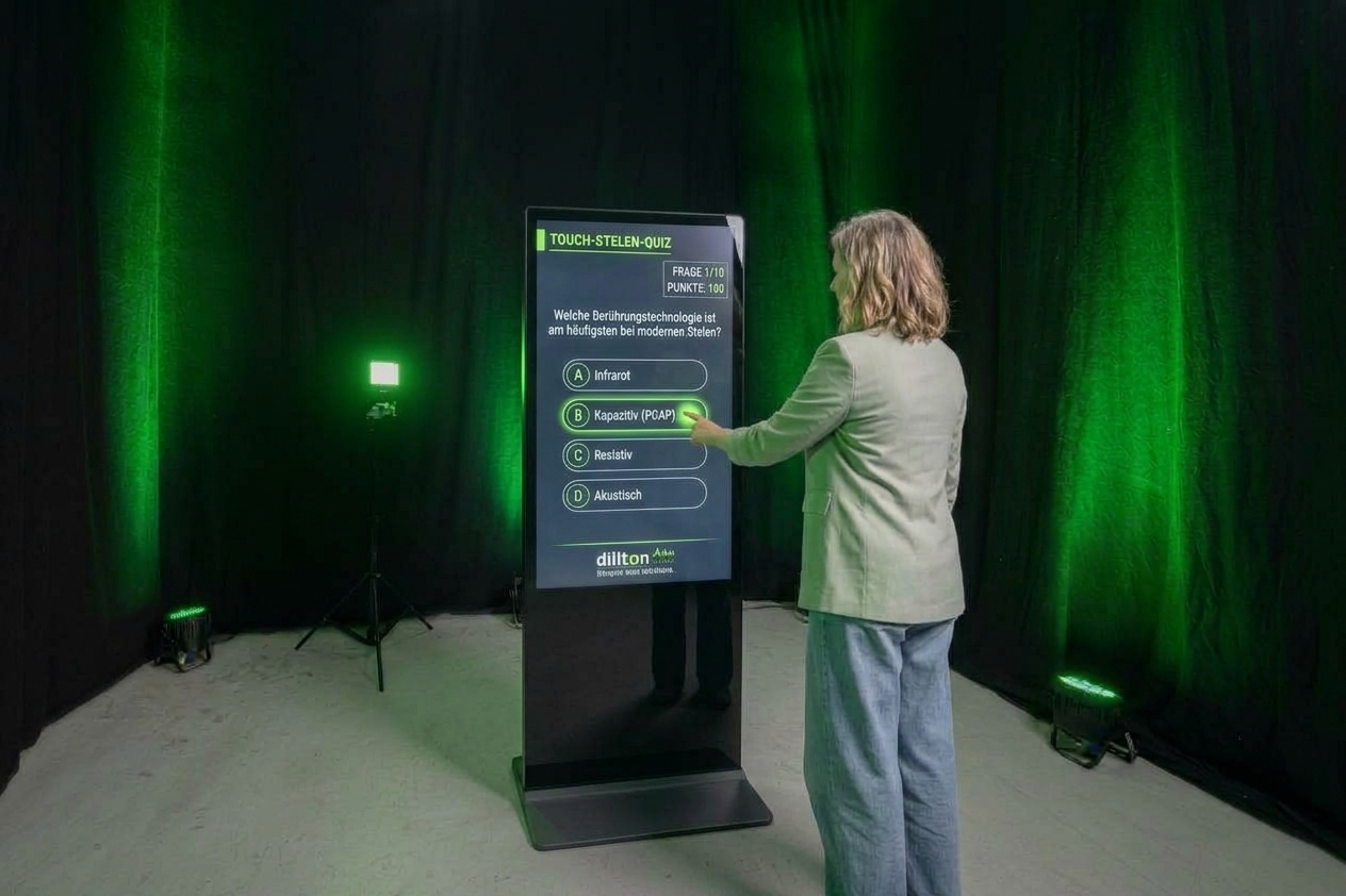 Eine Frau steht vor einer digitalen Touch-Stele auf einer Messe und beantwortet ein Multiple-Choice-Fach-Quiz vor einem grün beleuchteten Hintergrund.